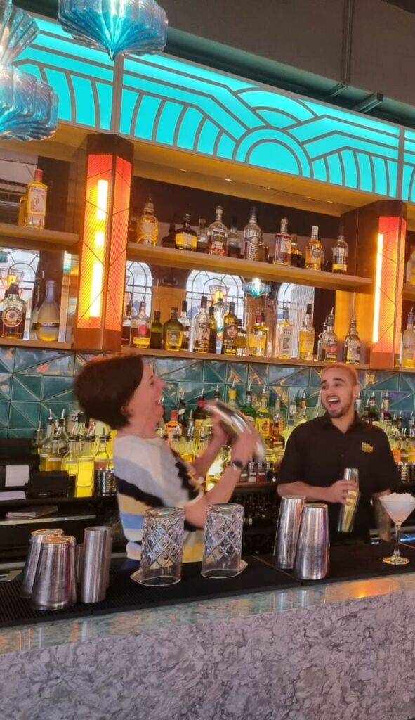 Paola shaking a cocktail mixer and laughing with the barman