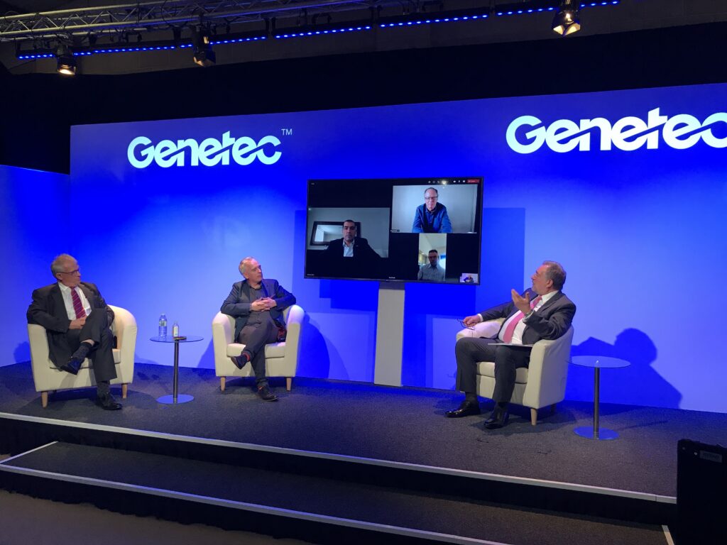 Hybrid event with people sat in chairs on a stage and also on a monitor screen in between them