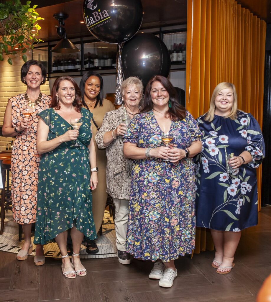 Paola, Vicky, Ashton, Vicki, Rebecca and Debbie standing, holding glasses of wine and smiling