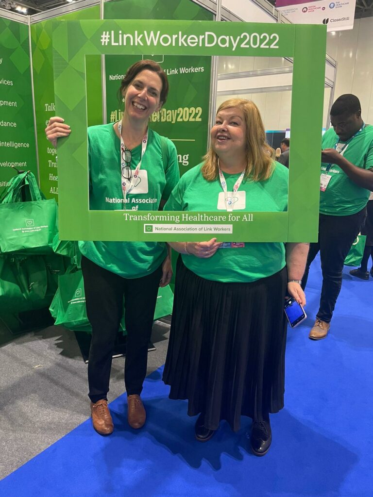 Paola and Debbie holding up a green selfie frame and smiling