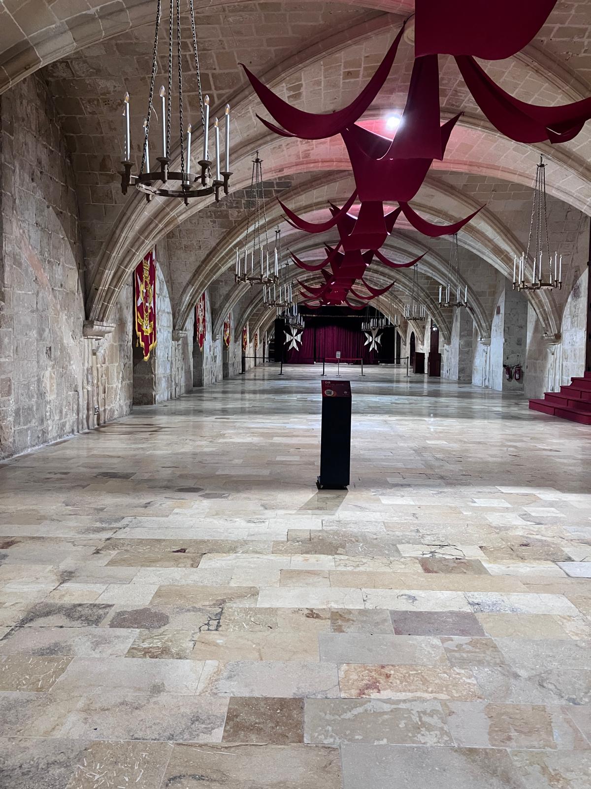 Medieval hall, vaulted stone ceiling and draped with burgendy material. Candle chandeliers.