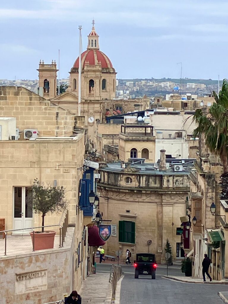 City view of typical street in Malta with old stone buildings. Sky is blue but cloudy