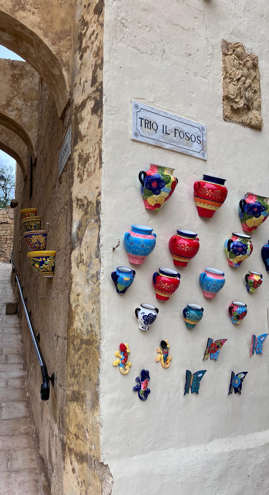 Colourful ceramic pots hanging on an house wall next to an archway path 